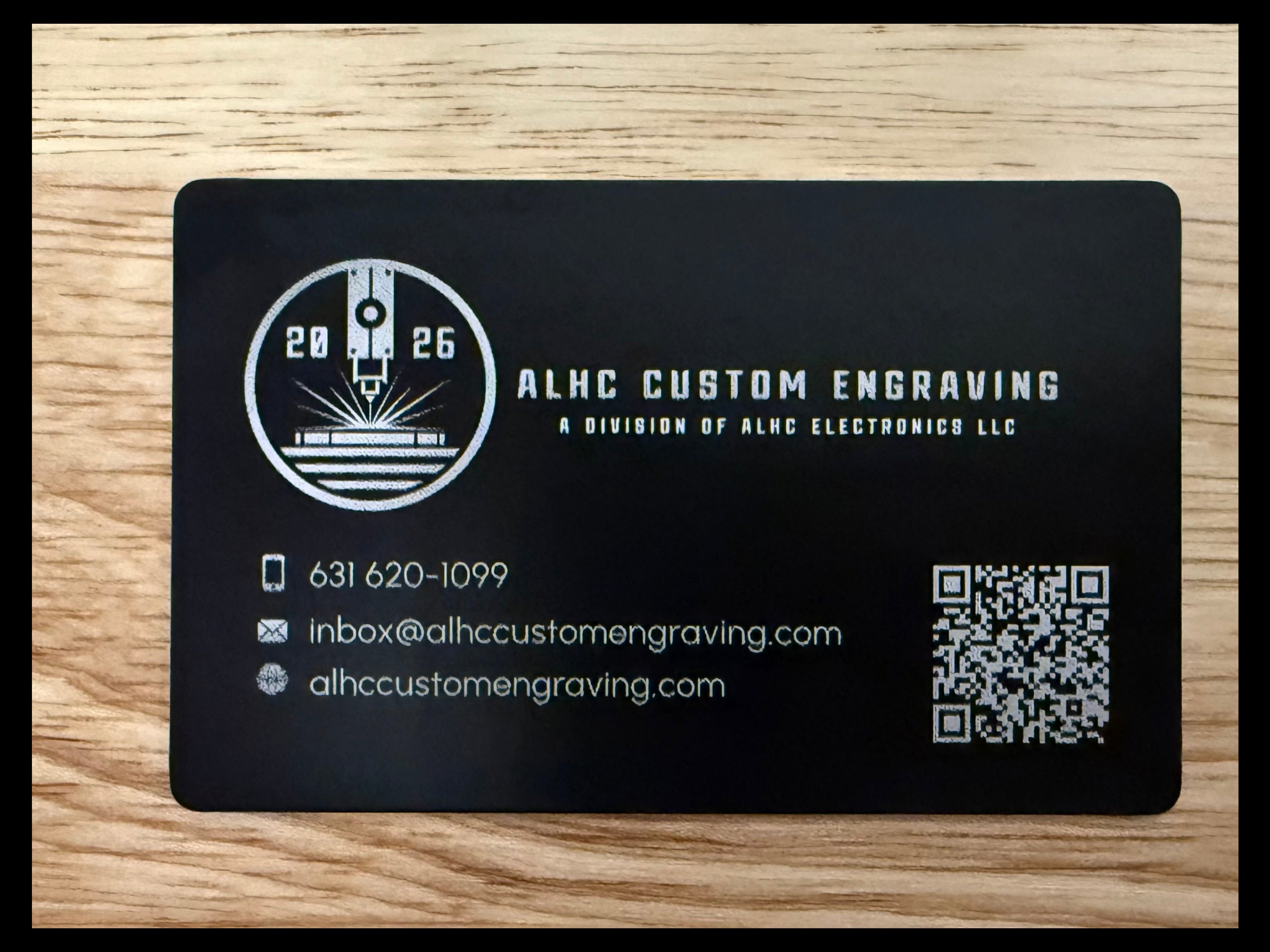 Black business card with white text and QR code on a wooden surface